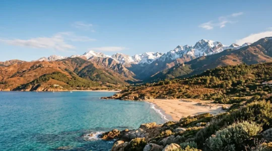 Paysage côtier corse avec montagne enneigée en arrière-plan visible depuis la plage