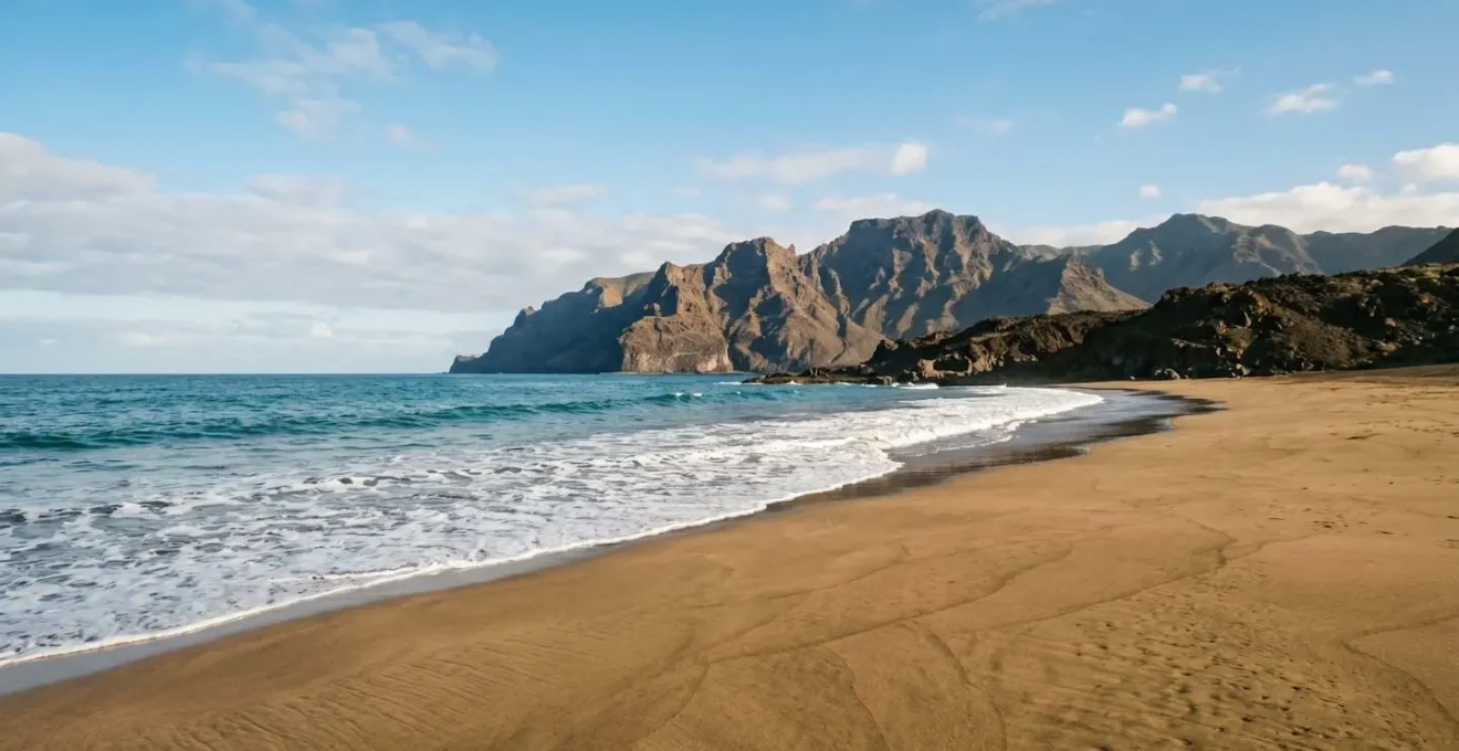Vue panoramique d'une plage canarienne ensoleillée avec relief volcanique en arrière-plan sous un ciel azur