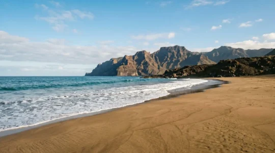 Vue panoramique d'une plage canarienne ensoleillée avec relief volcanique en arrière-plan sous un ciel azur