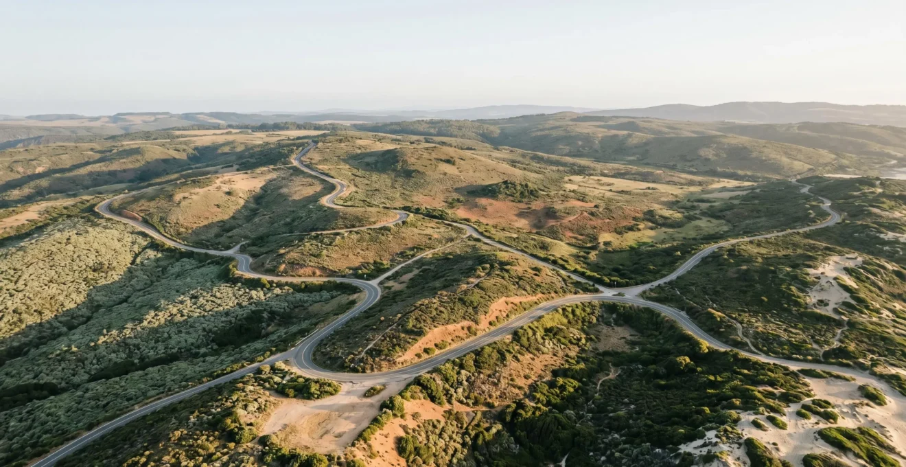 Vue aérienne minimaliste d'un réseau de routes sinueuses connectant plusieurs destinations à travers un paysage naturel épuré