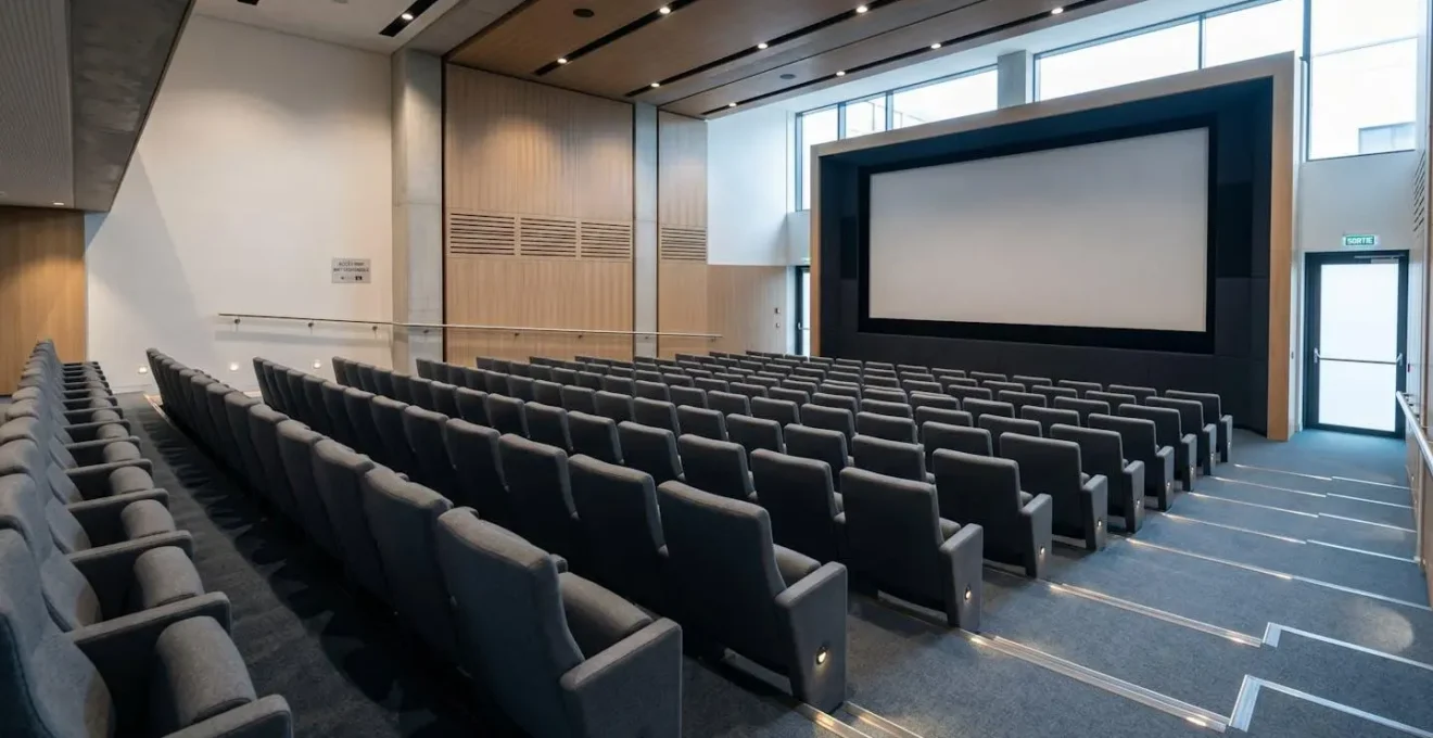 Auditorium moderne vide avec fauteuils en gradins orientés vers grand écran de projection, éclairage architectural professionnel, décor contemporain Luxembourg.